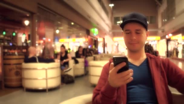 Maschio viaggiatore scorrimento app nel suo telefono cellulare al caffè dell'aeroporto. Clip 4K — Video Stock