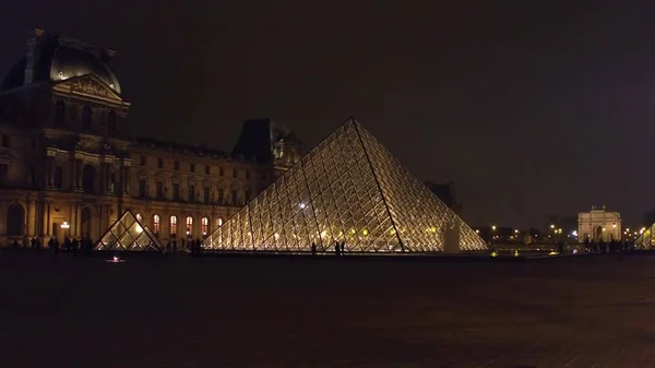PARIS, FRANÇA - DEZEMBRO, 31 de dezembro de 2016. Turistas silhuetas perto de vidro pirâmide do Louvre à noite. Famoso museu francês e destino turístico popular — Fotografia de Stock