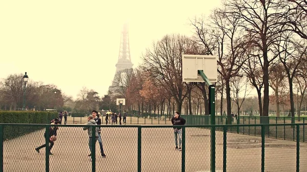 Paris, Frankrike -, 31 December 2016. Multinatonal manliga tonåringar spelar street basket mot Eiffeltornet på en dimmig dag, varma färger — Stockfoto