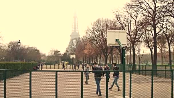 PARÍS, FRANCIA - 31 DE DICIEMBRE DE 2016. Adolescentes masculinos multinatonales jugando baloncesto callejero contra la Torre Eiffel en un día de niebla, colores cálidos. Clip 4K — Vídeo de stock