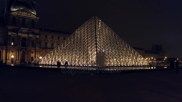 PARIS, FRANÇA - DEZEMBRO, 31 de dezembro de 2016. Turistas silhuetas perto de vidro pirâmide do Louvre à noite. Famoso museu francês e destino turístico popular. 4k steadicam vídeo — Vídeo de Stock