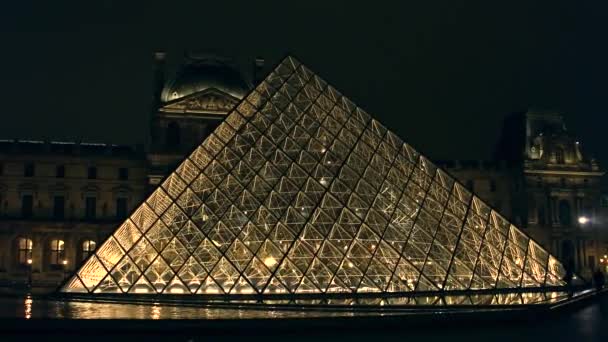 PARÍS, FRANCIA - 31 DE DICIEMBRE DE 2016. Los turistas siluetas cerca de vidrio pirámide del Louvre por la noche. Famoso museo francés y popular destino turístico. Clip steadicam 4k — Vídeo de stock