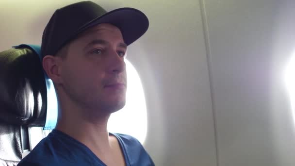 Молодой задумчивый кавказский человек путешествует на самолёте. 4K видео крупным планом — стоковое видео
