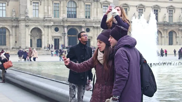 PARIS, FRANÇA - DEZEMBRO, 31 de dezembro de 2016. Casais multiétnicos fazendo selfies perto da pirâmide de vidro do Louvre e fontes. Famoso museu francês, popular destino turístico — Fotografia de Stock
