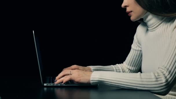 Attraktiv brunett kvinna att skriva på hennes bärbara dator mot mörk bakgrund. 4k-video — Stockvideo
