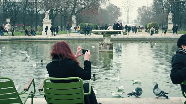 Paris, Frankreich - 31. Dezember 2016. Frau macht Fotos von schönen Teich im Park gegen Riesenrad. Beliebtes Pariser Wahrzeichen und touristisches Ziel — Stockfoto