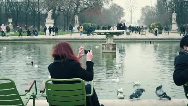 ПАРИЖ, ФРАНЦИЯ - 31 ДЕКАБРЯ 2016 года. Женщина делает фотографии прекрасного пруда в парке против колеса обозрения. Популярная парижская достопримечательность и туристическое направление. 4K видео — стоковое видео