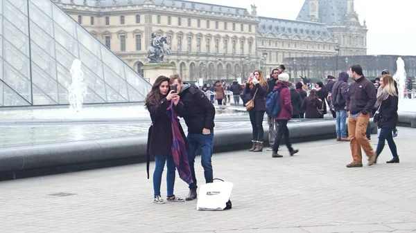 PARIS, FRANÇA - DEZEMBRO, 31 de dezembro de 2016. Steadicam tiro de casal fazendo selfie perto da pirâmide de vidro do Louvre e fontes. Famoso museu francês, popular destino turístico — Fotografia de Stock