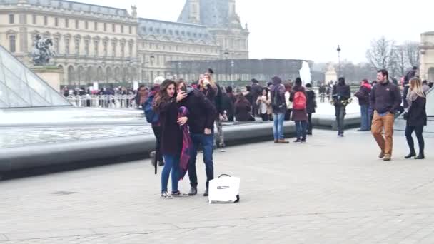 PARÍS, FRANCIA - 31 DE DICIEMBRE DE 2016. Steadicam disparo de pareja haciendo selfie cerca de la pirámide de vidrio del Louvre y fuentes. Famoso museo francés y popular destino turístico. Vídeo 4K — Vídeo de stock