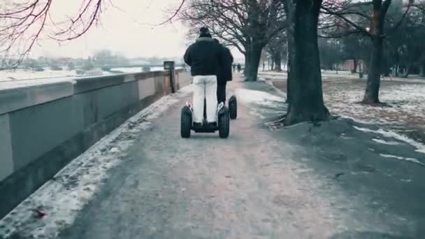 Стедикам снял двух неузнаваемых мужчин, путешествующих зимой по сегвеям вдоль набережной реки. 4K видео — стоковое видео