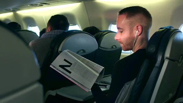 WARSAW, POLONIA - 24 DE DICIEMBRE DE 2016. Joven escuchando la revista de música y lectura en cabina de avión — Foto de Stock