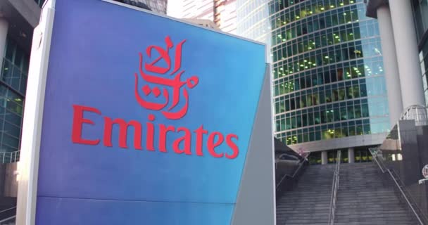 Уличная вывеска с логотипом Emirates Airline. Современный офисный центр небоскреб и лестница фон. 3D-рендеринг в 4K — стоковое видео