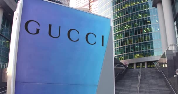 Cartelera con logotipo de Gucci. Rascacielos moderno centro de oficina y escaleras de fondo. Editorial 3D renderizado 4K — Vídeos de Stock