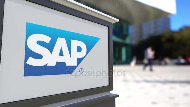 Tablero de señalización con logotipo de SAP SE. Centro de oficina borrosa y gente caminando fondo. Editorial 3D renderizado 4K — Vídeos de Stock