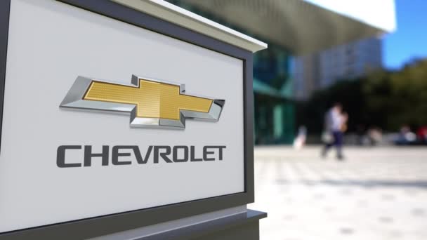 Tablero de señalización con el logotipo de Chevrolet. Centro de oficina borrosa y gente caminando fondo. Editorial 3D renderizado 4K — Vídeo de stock