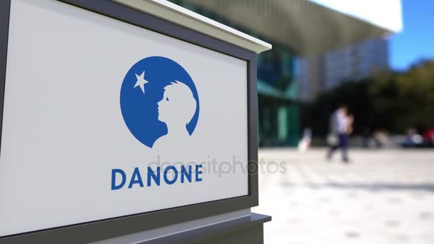 Уличная вывеска с логотипом Danone. Размытый офисный центр и ходячий фон. 3D-рендеринг в 4K — стоковое видео