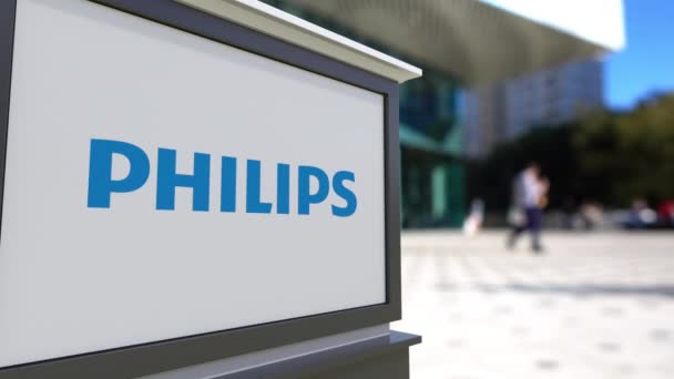 Уличная вывеска с логотипом Philips. Размытый офисный центр и ходячий фон. 3D-рендеринг в 4K — стоковое видео
