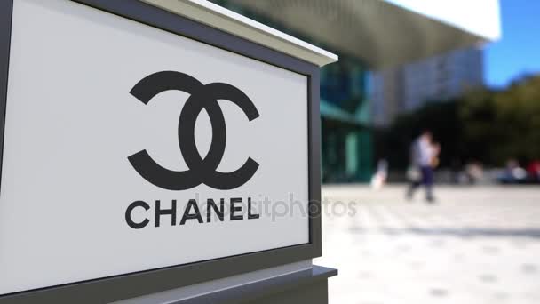 Уличная вывеска с логотипом Шанель. Размытый офисный центр и ходячий фон. 3D-рендеринг в 4K — стоковое видео