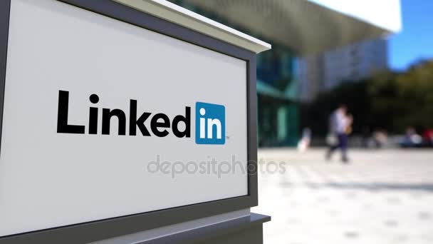 Tablero de señalización con logotipo de LinkedIn. Centro de oficina borrosa y gente caminando fondo. Editorial 3D renderizado 4K — Vídeos de Stock