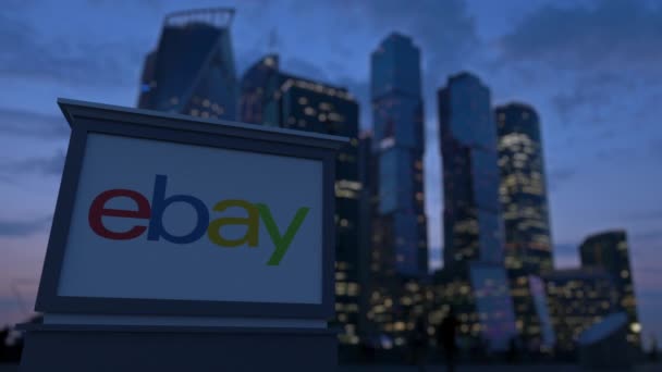 Tablero de la señalización de la calle con el logotipo de eBay Inc. en la noche. Rascacielos distritos de negocios borrosa fondo. Editorial 3D renderizado 4K — Vídeo de stock