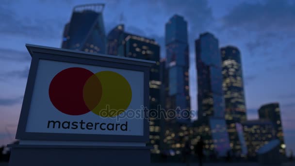 Straat signalisatie bord met Mastercard-logo in de avond. Zakelijke district wolkenkrabbers achtergrond wazig. Redactionele 3d rendering van 4k — Stockvideo