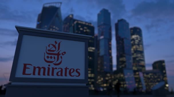 Panneau de signalisation avec logo Emirates Airline le soir. Fond flou de gratte-ciel de quartier d'affaires. Editorial 3D rendu 4K — Video
