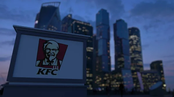 Уличная вывеска с логотипом Kentucky Fried Chicken KFC вечером. Размытые данные о небоскребах в деловом районе. Редакционная 3D рендеринг — стоковое фото