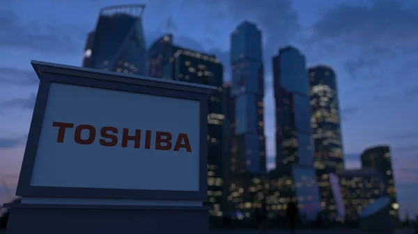 Pouliční nápisy deska s logem Toshiba Corporation ve večerních hodinách. Obchodní čtvrť mrakodrapů pozadí rozmazané. Úvodník 3d vykreslování — Stock fotografie