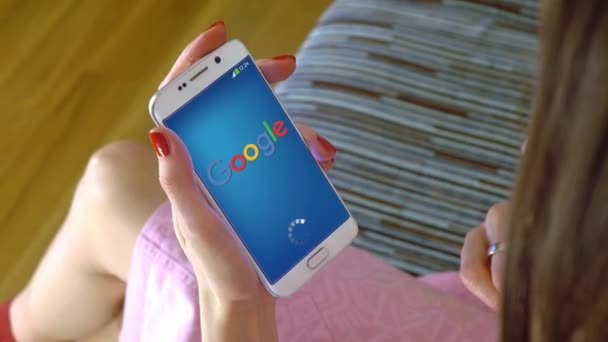Ung kvinna som håller en mobiltelefon med lastning Google mobila app. konceptuell redaktionella 4k klipp — Stockvideo