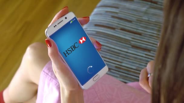 Jeune femme tenant un téléphone portable avec chargement de l'application mobile HSBC. Clip conceptuel éditorial 4K — Video
