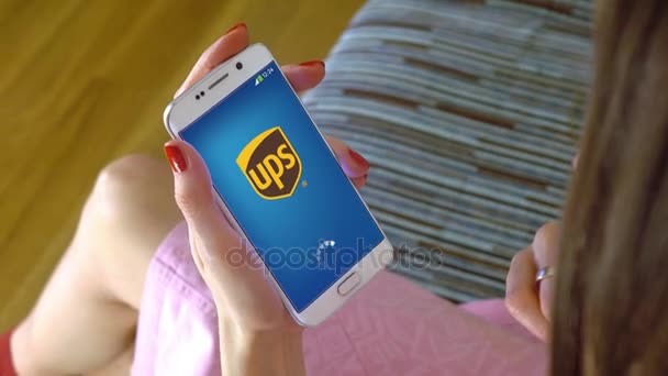 Mujer joven sosteniendo un teléfono celular con la carga de la aplicación móvil UPS. Editorial conceptual 4K clip — Vídeo de stock