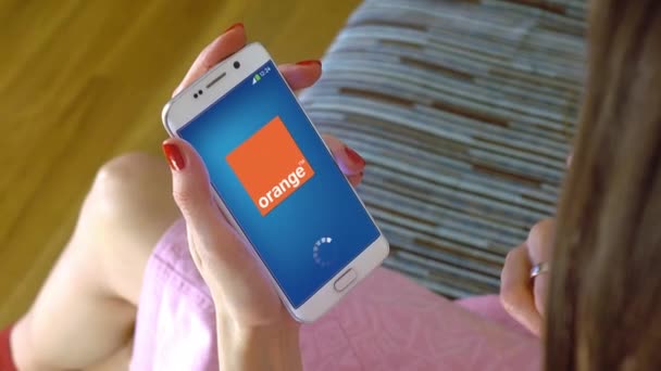 Giovane donna in possesso di un telefono cellulare con caricamento app mobile Orange. Clip editoriale concettuale 4K — Video Stock