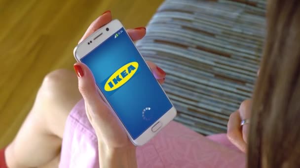 Wanita muda memegang ponsel dengan memuat aplikasi ponsel Ikea. Clip editorial konseptual 4K — Stok Video