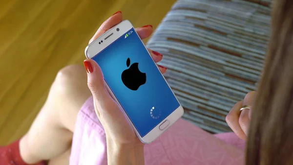 Mujer joven sosteniendo un teléfono celular con la carga de la aplicación móvil Apple. Editorial conceptual CGI — Foto de Stock