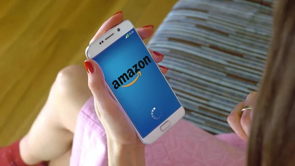 Jovem segurando um telefone celular com o carregamento do aplicativo móvel Amazon. Editorial conceitual CGI — Fotografia de Stock