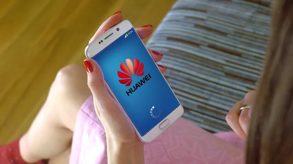 Молодая женщина держит мобильный телефон с загрузкой Huawei мобильного приложения. Концептуальная редакционная CGI — стоковое фото