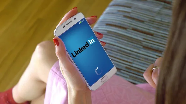 Mujer joven sosteniendo un teléfono celular con la carga de la aplicación móvil LinkedIn. Editorial conceptual CGI — Foto de Stock