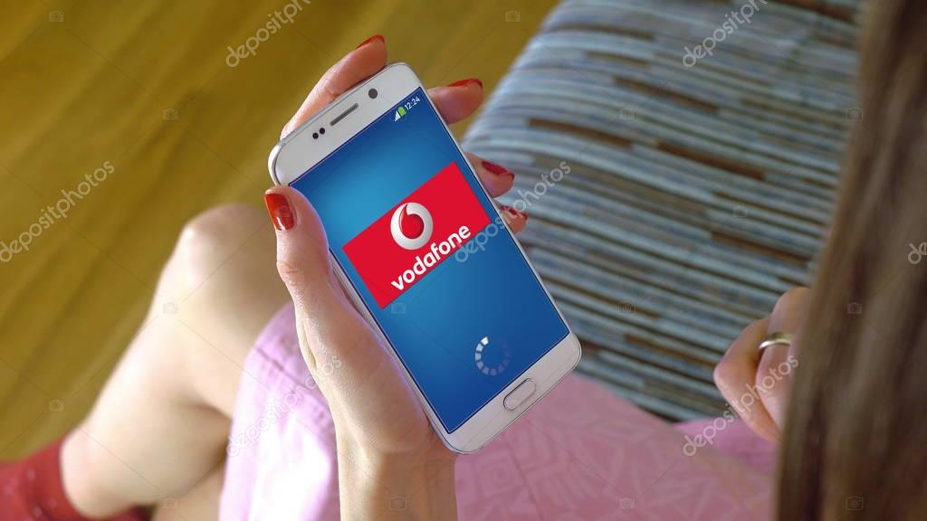 Young woman holding a cell phone with loading Vodafone mobile app. Conceptual editorial image