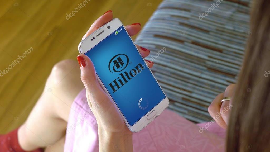 Young woman holding a cell phone with loading Hilton mobile app. Conceptual editorial image