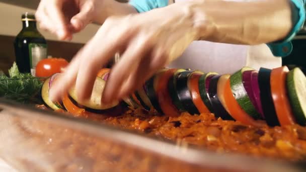 Молодая женщина кладет нарезанные овощи в стеклянную сковороду. Любительская кухня домашнего рататуя. 4К выстрел — стоковое видео