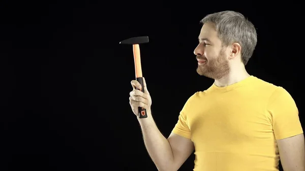 Hombre alegre en camiseta amarilla sostiene martillo. Conceptos de bricolaje, reparación, construcción amateur o mejora del hogar. Fondo negro — Foto de Stock