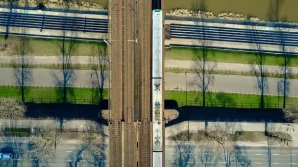 Plano aéreo del tren de pasajeros que se mueve en el puente ferroviario a través del río, carretera en bicicleta y carretera, vista superior. Vídeo 4K — Vídeos de Stock