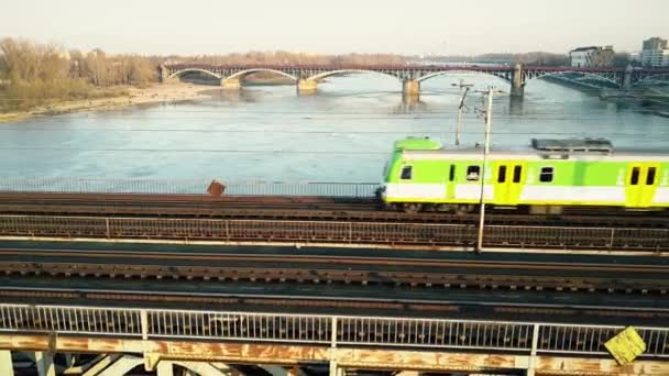 Воздушный кадр зелёного и жёлтого пассажирского поезда, движущегося по железнодорожному мосту через реку. 4K видео — стоковое видео