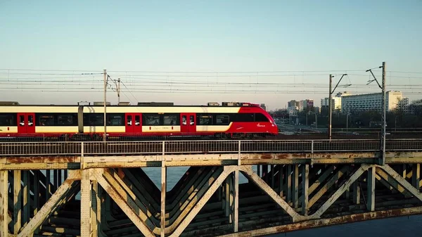 Varsó, Lengyelország - március, 27, 2017. Légi felvétel piros személyszállító vonat halad a vasúti híd a folyón — Stock Fotó