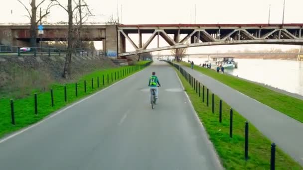 Luchtfoto tracking shot van jonge man met rugzak paardrijden zijn fiets langs de rivier Dijk avond. 4 k-clip — Stockvideo