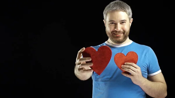 Hombre barbudo sonriente en camiseta azul dando forma de corazón rojo. Amor, romance, citas, conceptos de propuesta. Fondo negro — Foto de Stock