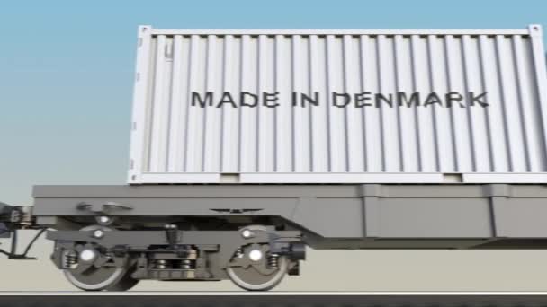 Tren de carga en movimiento y contenedores con leyenda MADE IN DINAMARK. Transporte ferroviario. Clip 4K de bucle sin costura — Vídeos de Stock