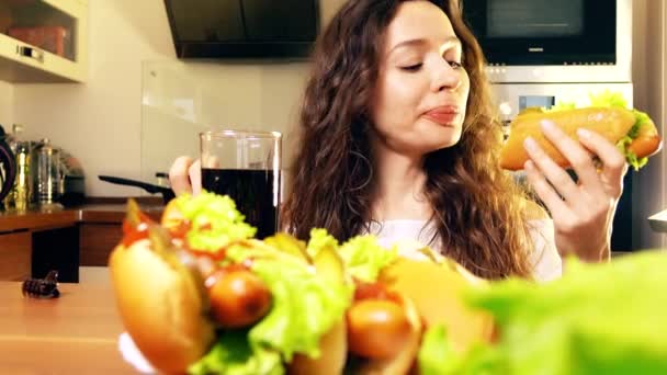 Όμορφη μελαχρινή νεαρή γυναίκα τρώει χοτ-ντογκ και πόσιμο cola στο σπίτι. Έννοια junk food. βίντεο 4k — Αρχείο Βίντεο