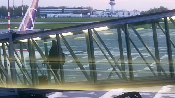 Passagier lopen in een glazen jet-brug. Aan boord van een vliegtuig op de luchthaven in de avond — Stockfoto