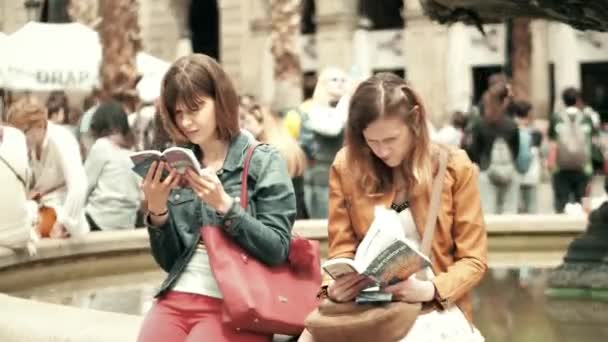 Βαρκελώνη, Ισπανία - Απριλίου 16, 2017. Δύο νεαρές γυναίκες διαβάζοντας βιβλία οδηγός τουριστική πόλη κοντά στη βρύση. βίντεο 4k — Αρχείο Βίντεο